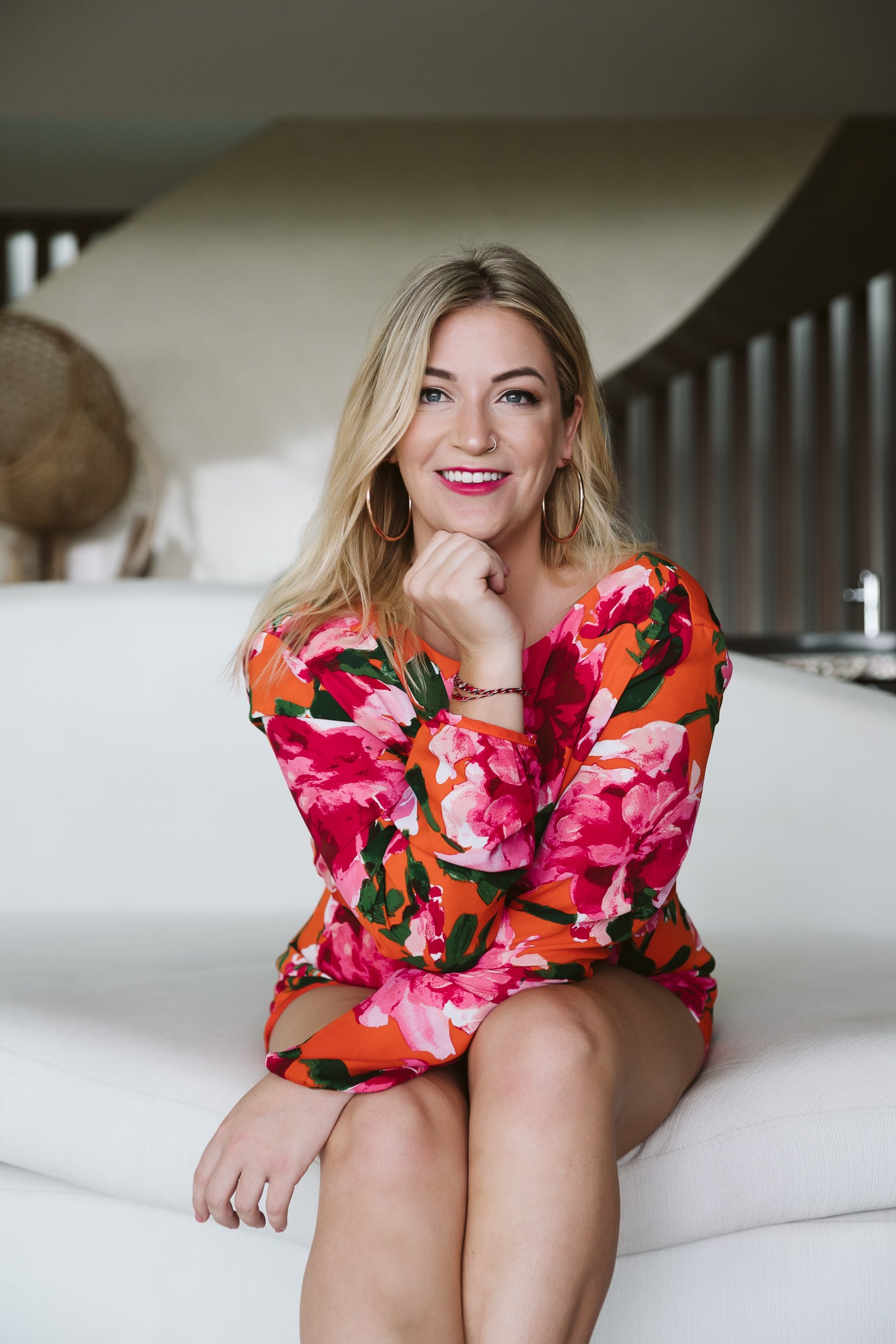 Woman in a colorful floral dress sitting on a white couch.