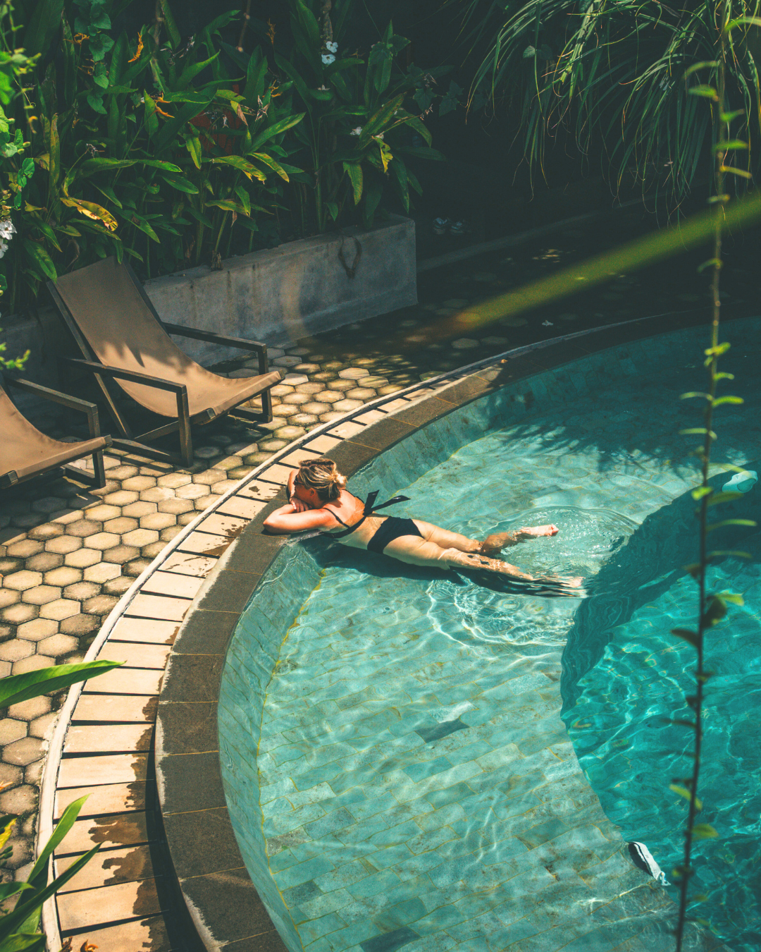 Person lounging by a pool with greenery around