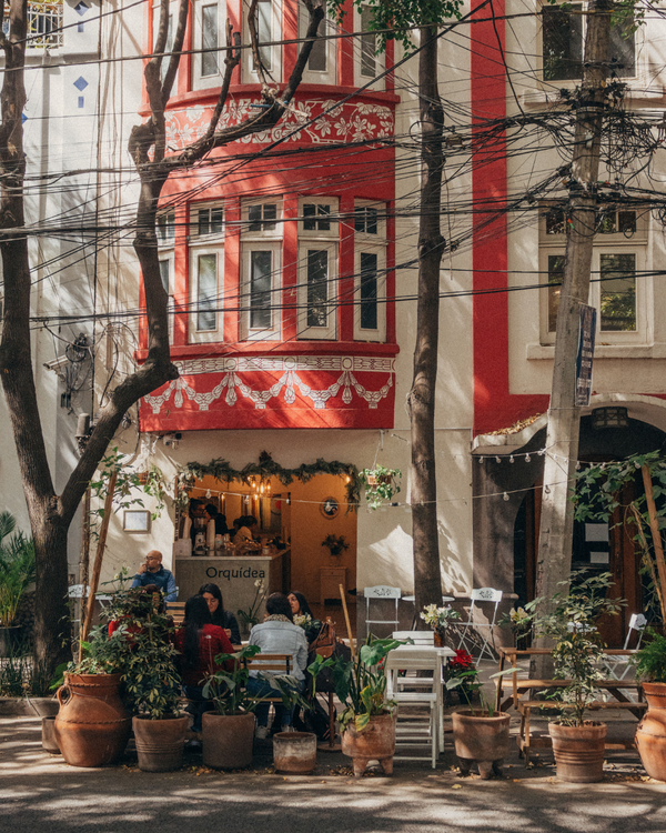 Street scene with a red building facade and outdoor seating area with plants.
