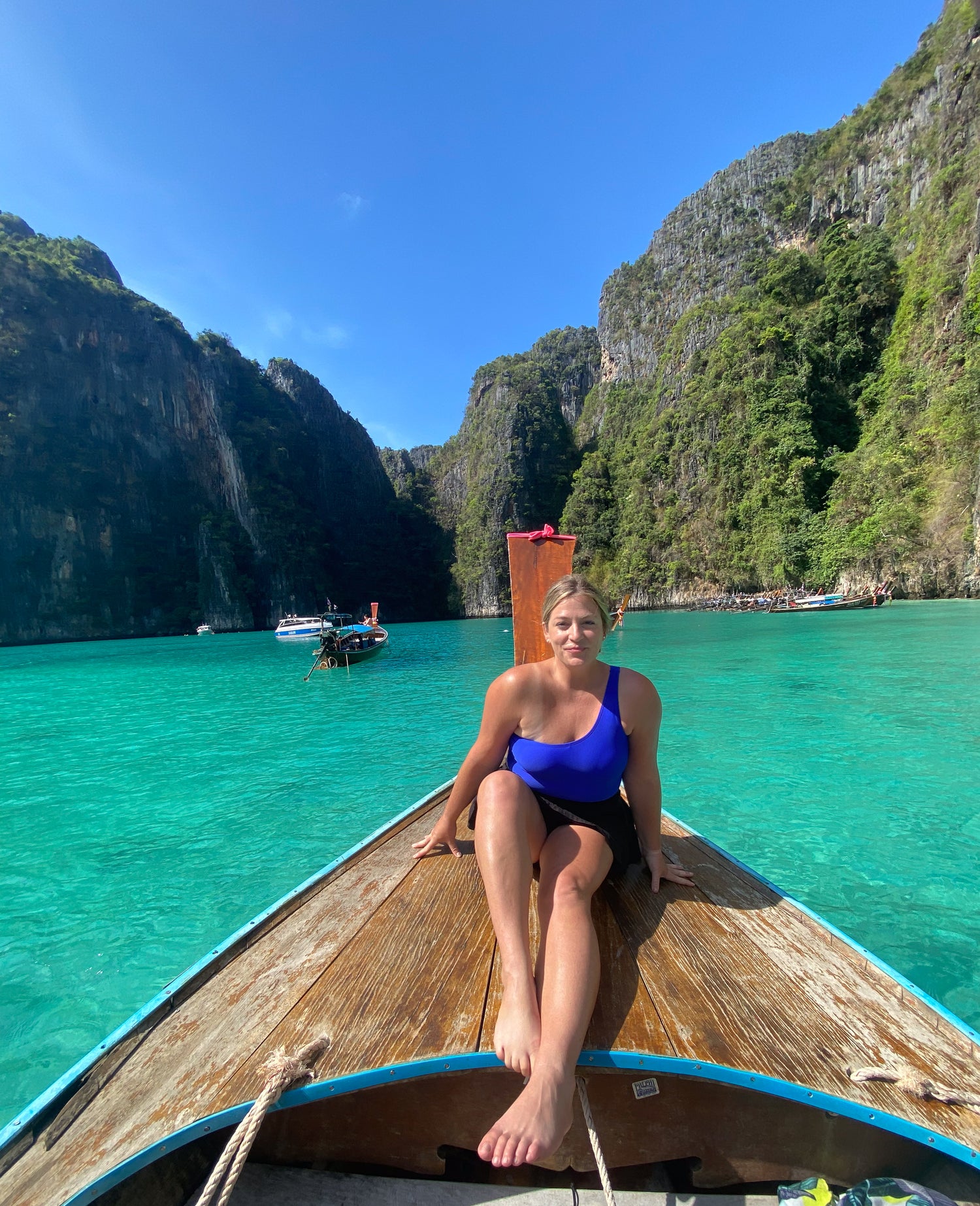 Woman in a blue swimsuit sitting on a longtail boat with turquoise water and cliffs in the background