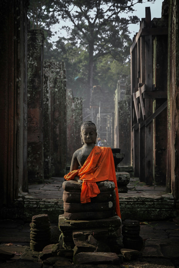 Monk in orange robe sitting on stone steps in a temple setting in Cambodia