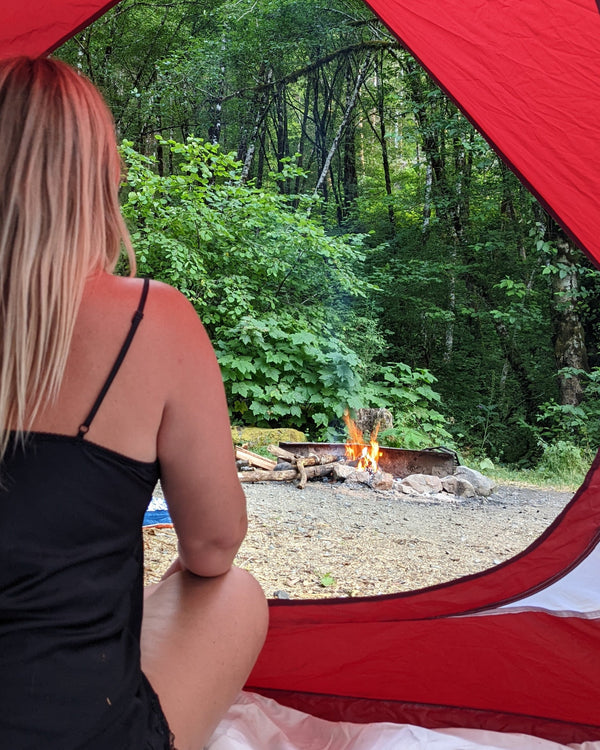 Person sitting inside a red tent looking at a campfire in the woods