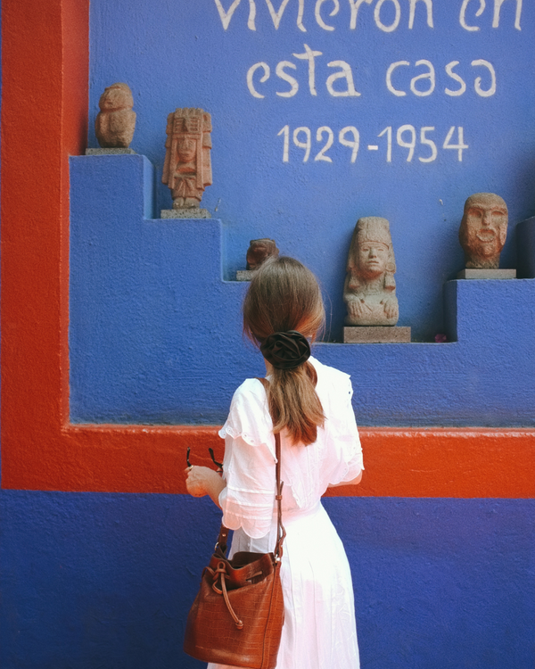 Woman in a white dress standing in front of a colorful wall with statues and text.