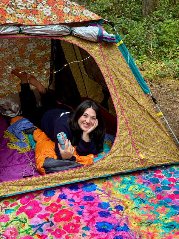 Person lying inside a colorful tent with floral patterns in a forest setting in Seattle