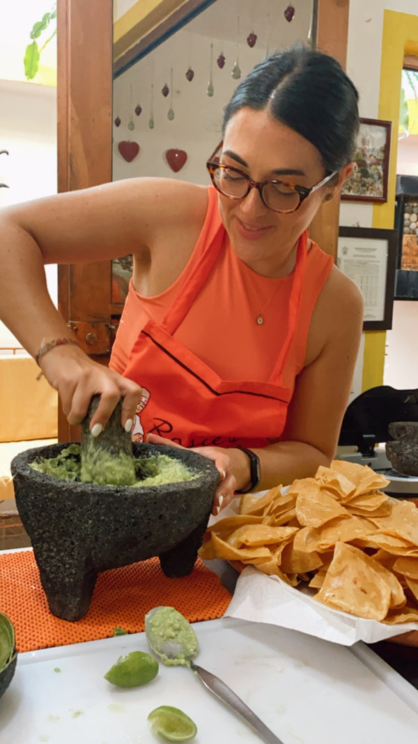 Woman in an orange shirt preparing food at a table with tortilla chips and limes.