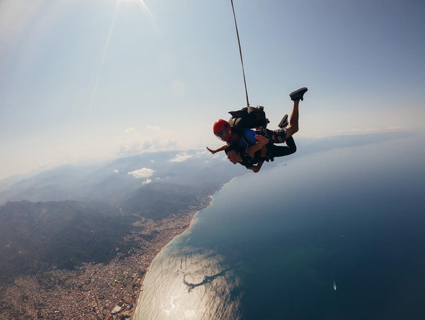 Two people paragliding over a coastal landscape with a clear sky.