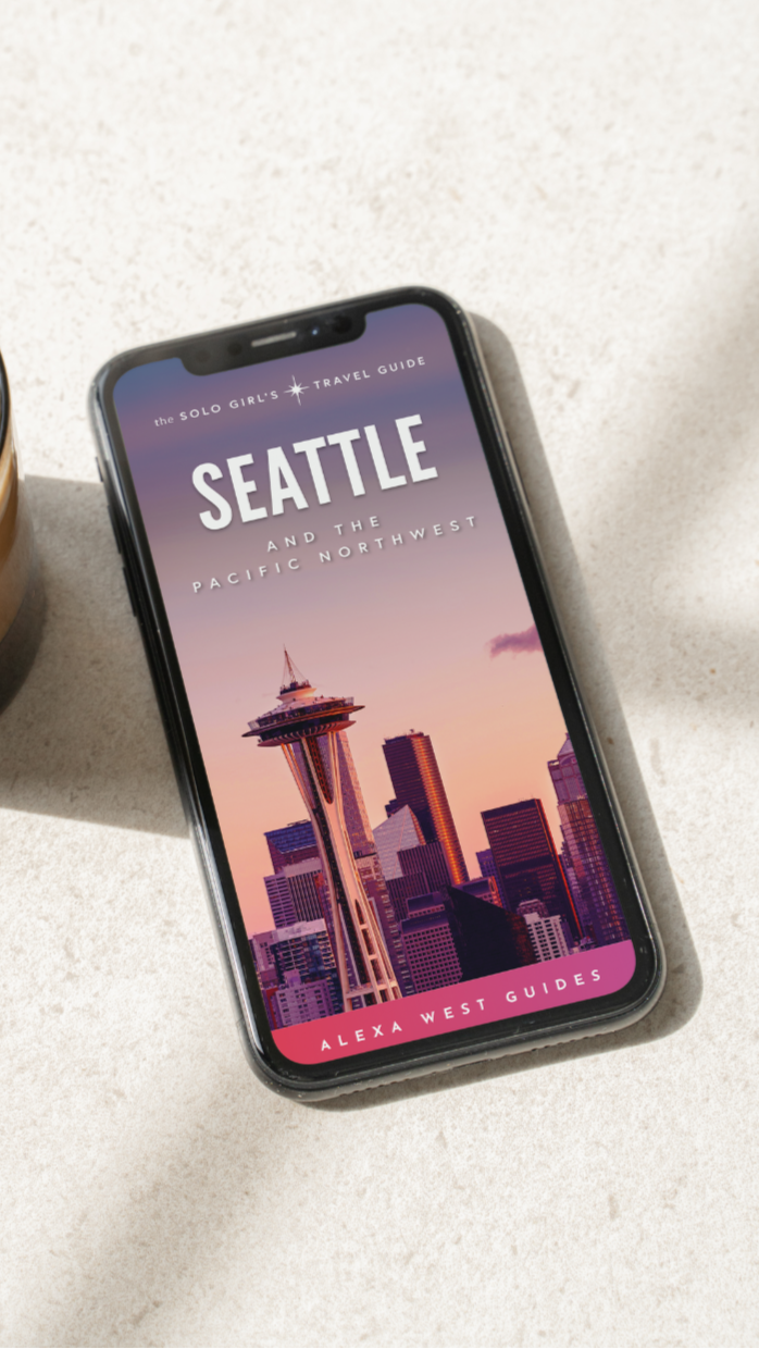 Phone displaying a Seattle-themed app with a city skyline on a light surface next to a coffee cup.
