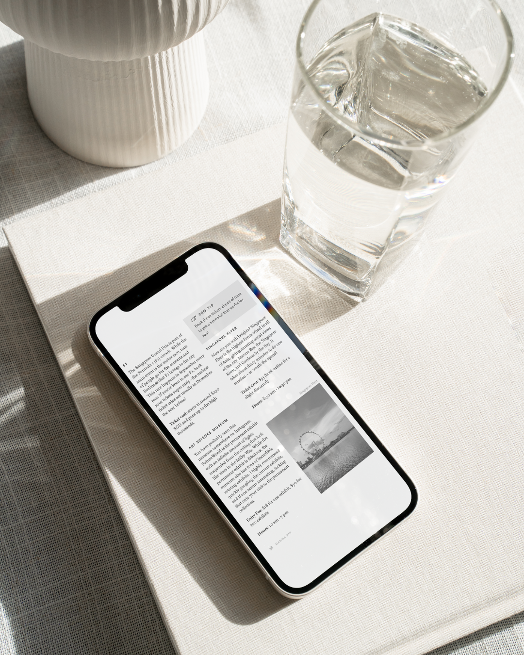 Phone displaying a webpage on a white surface with a glass of water and a vase.