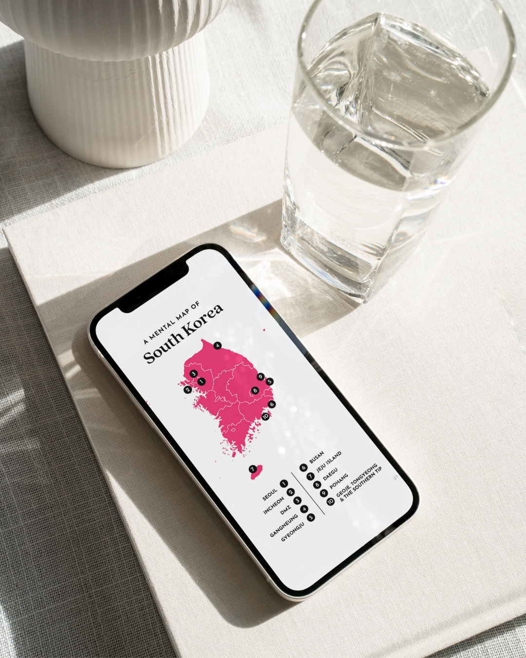 Phone displaying a map of South Korea on a light surface with a glass of water and decorative items.