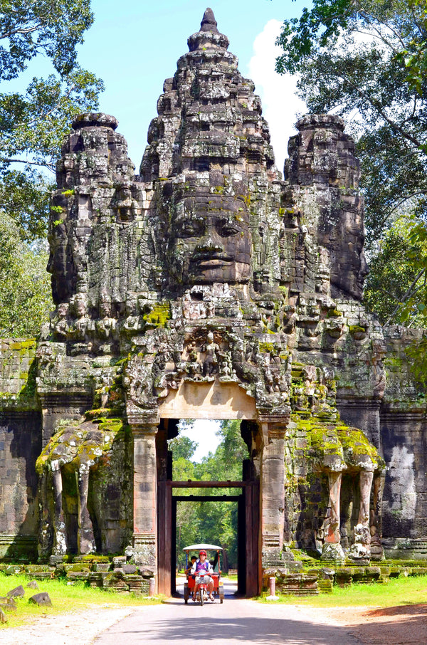Stone temple gate with face and elephant carvings in a lush green setting