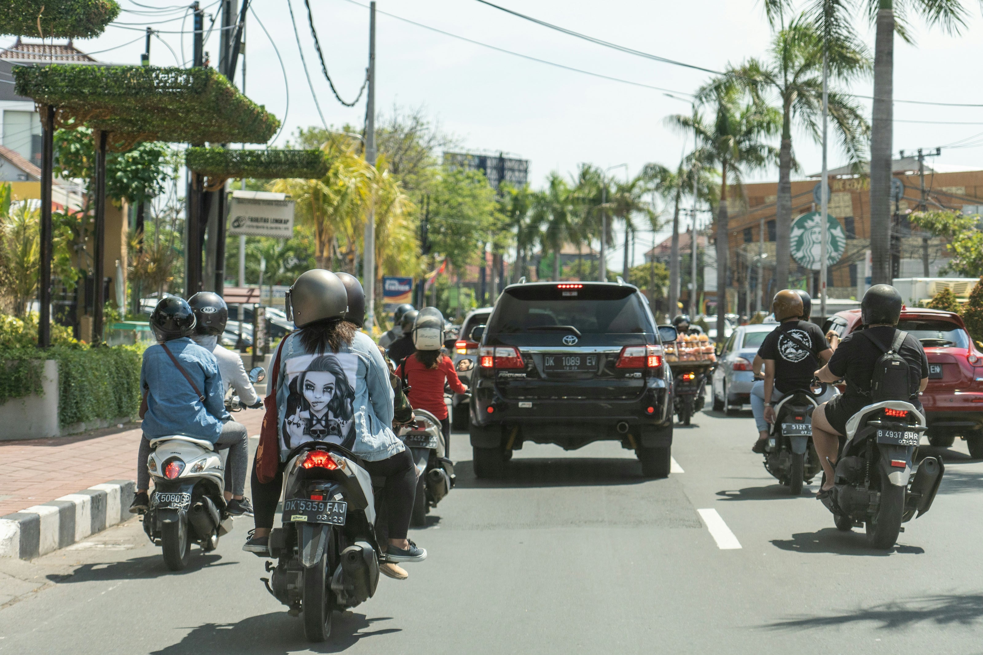 People riding motorcycles and cars on a city street.
