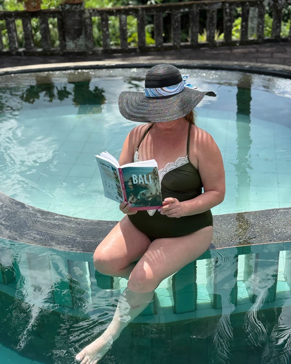 Woman reading a book by a pool with a scenic background