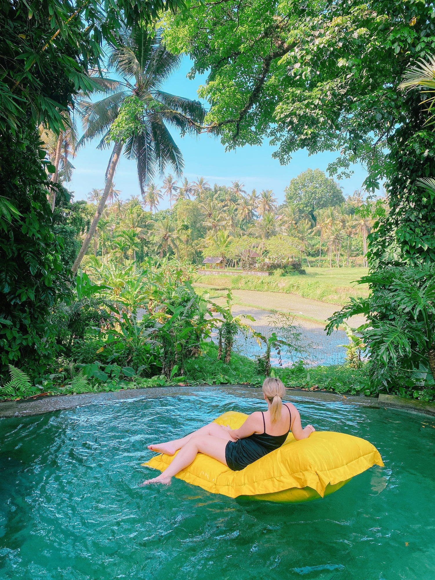 Person lounging on a yellow inflatable raft in a pool surrounded by lush greenery in Bali