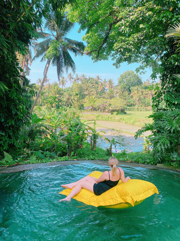 Person lounging on a yellow inflatable raft in a pool surrounded by lush greenery in Bali