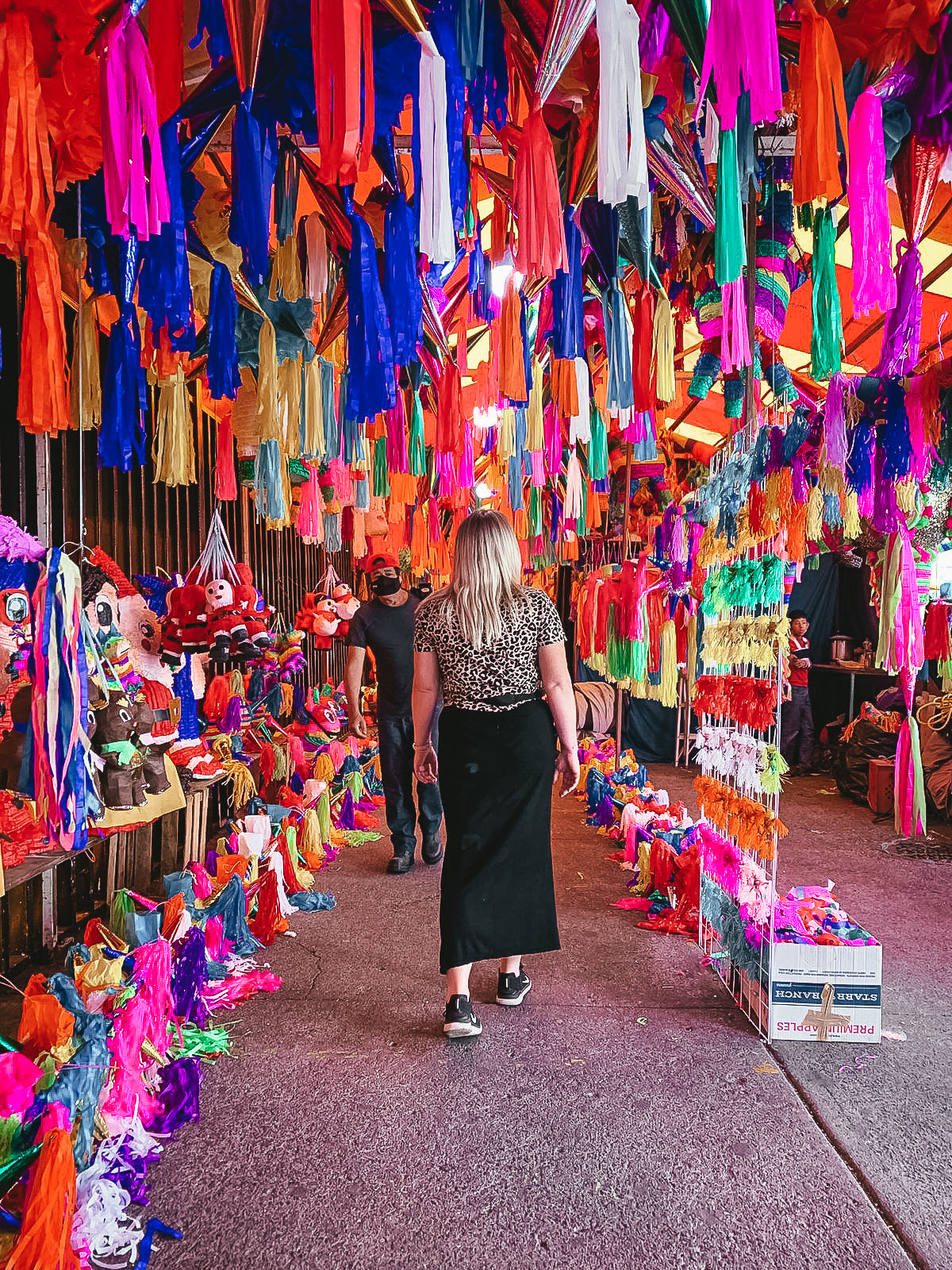 Woman walking through a colorful market stall with hanging decorations