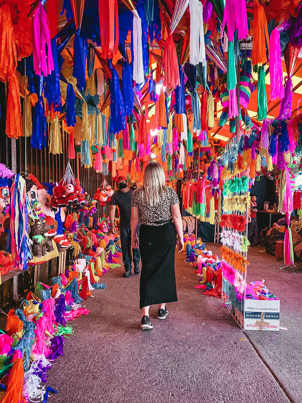 Woman walking through a colorful market stall with hanging decorations
