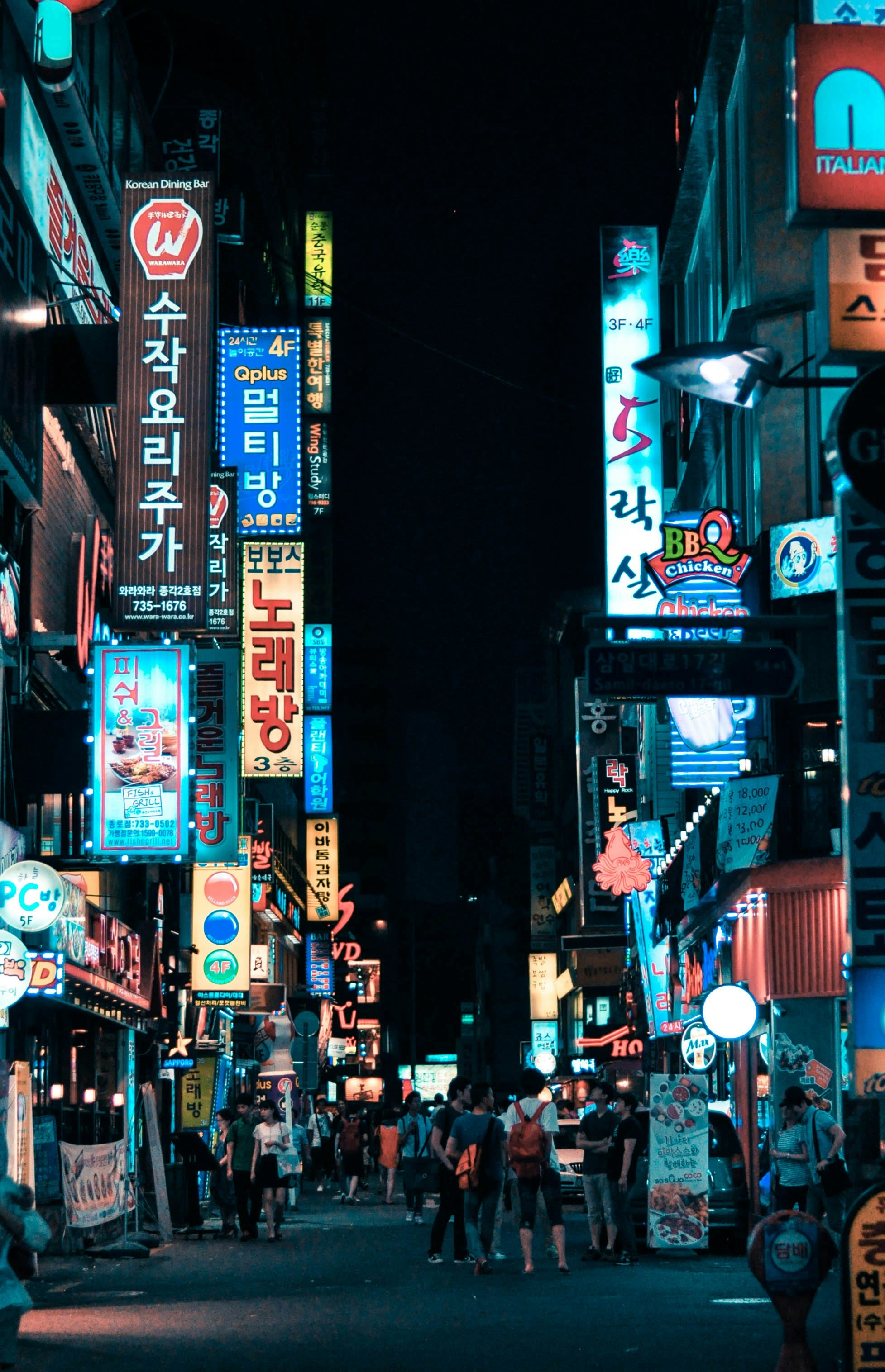 Neon-lit street scene in a city at night with various signs and advertisements.