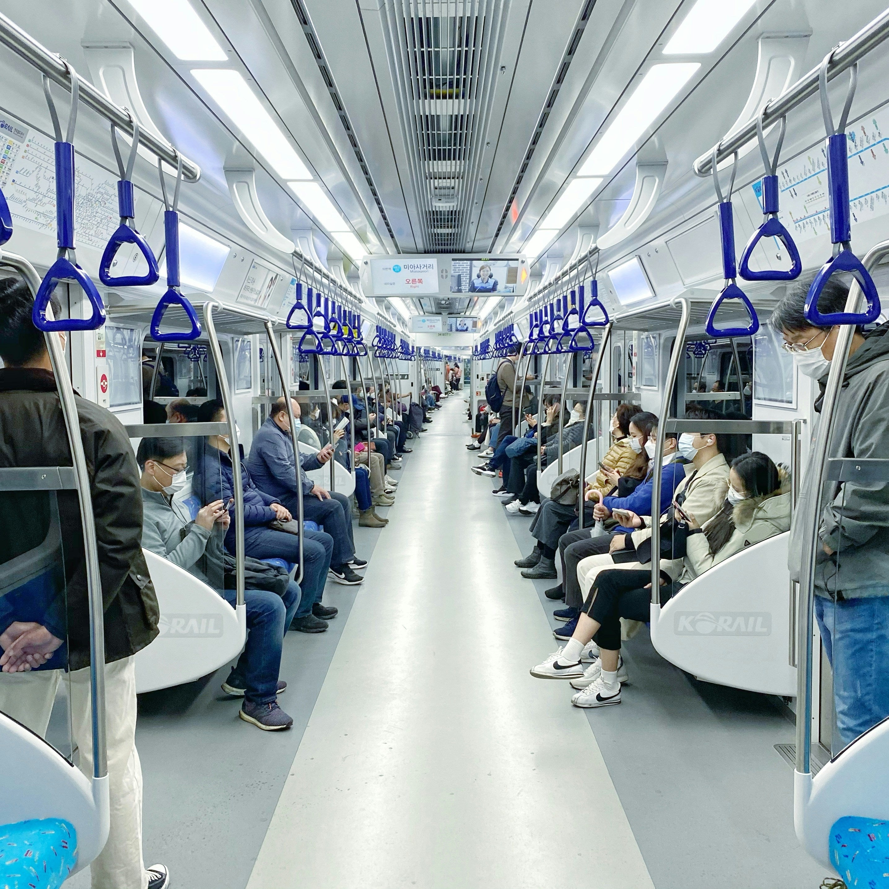 People sitting on a modern subway train with blue handrails.