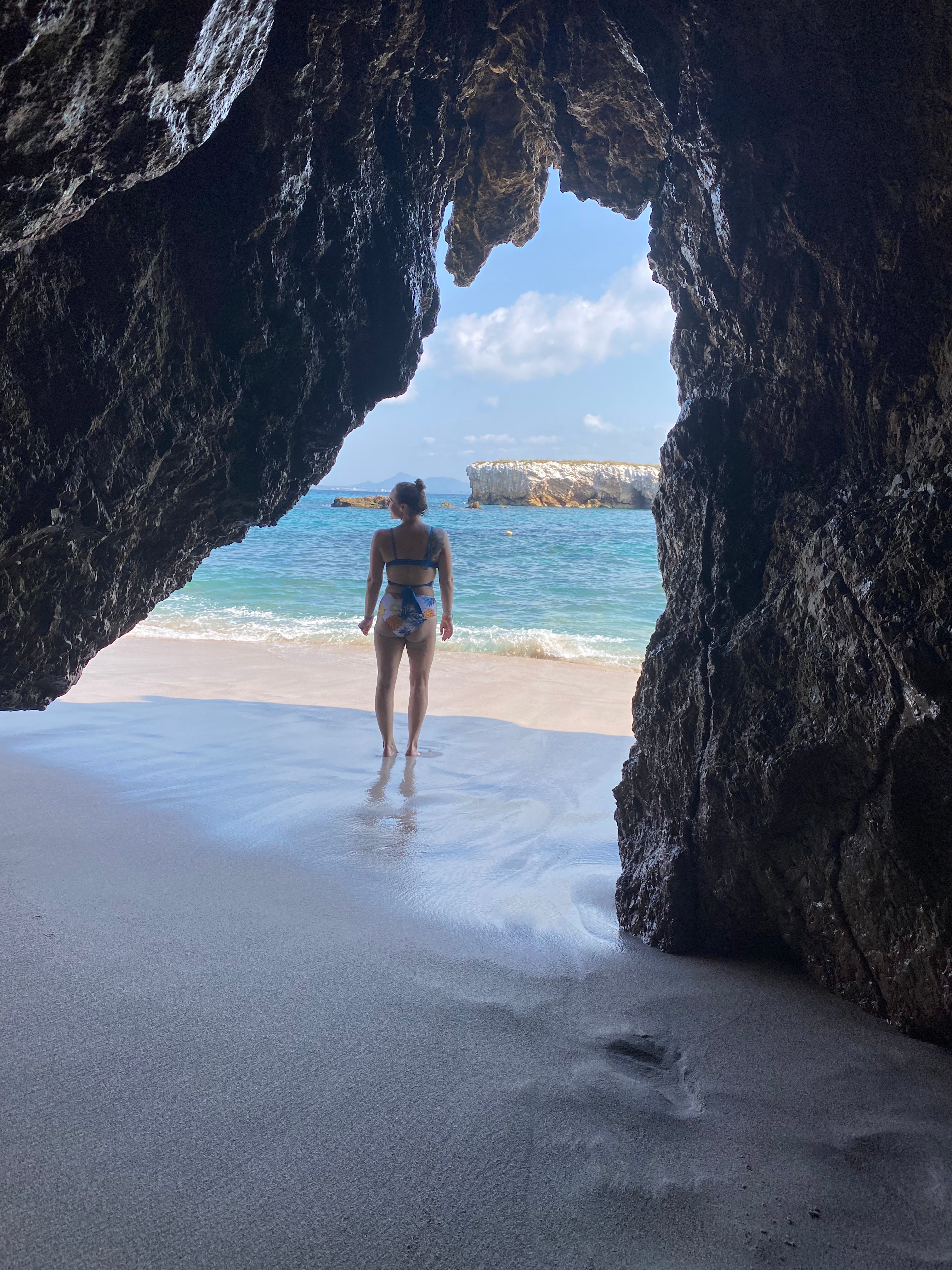 Person standing inside a cave on a beach with ocean view