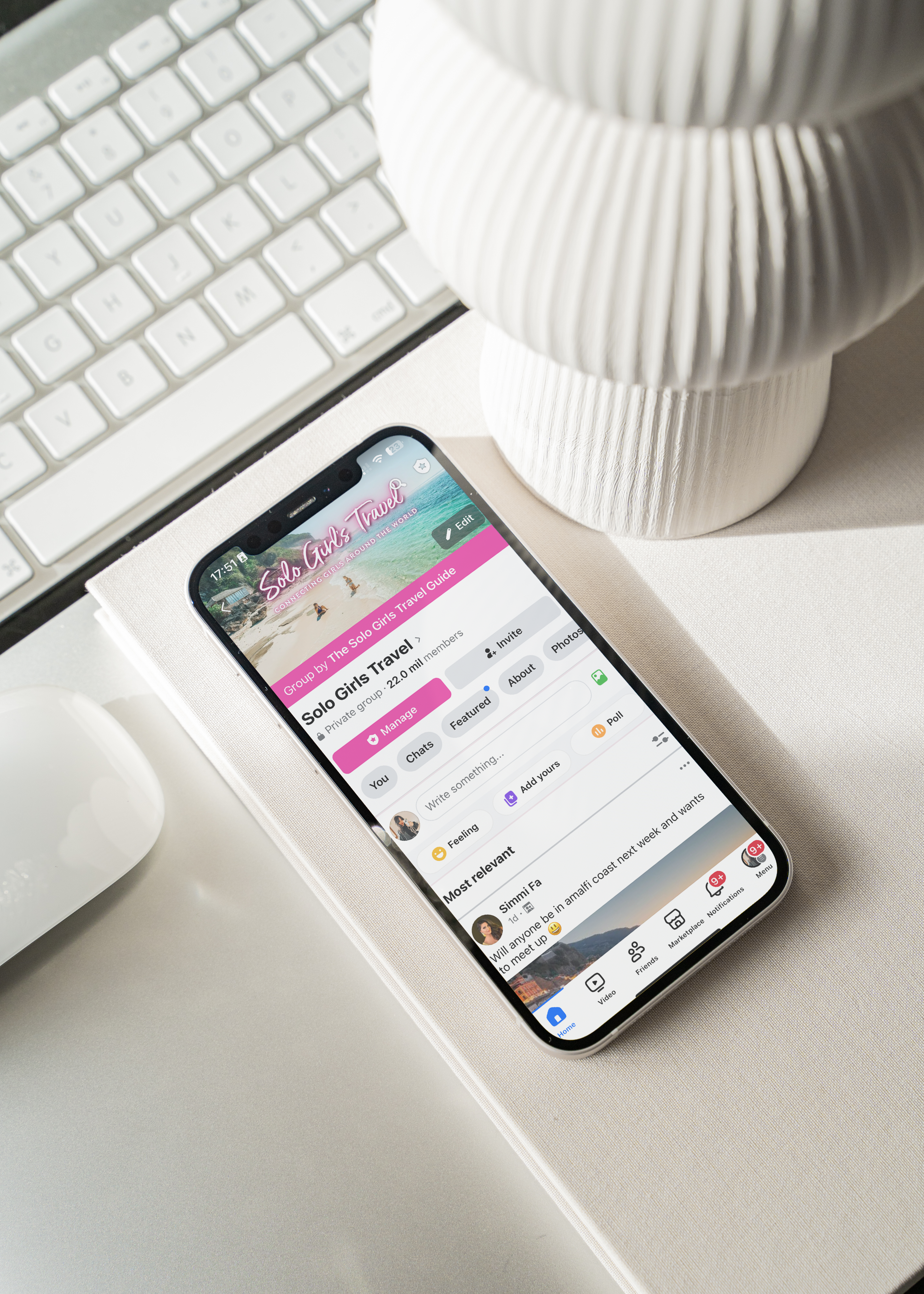 Smartphone displaying a social media app on a desk with a keyboard and decorative vase.
