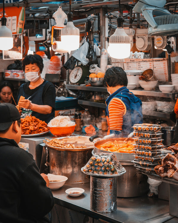 People working in a bustling market kitchen with various food items and utensils.