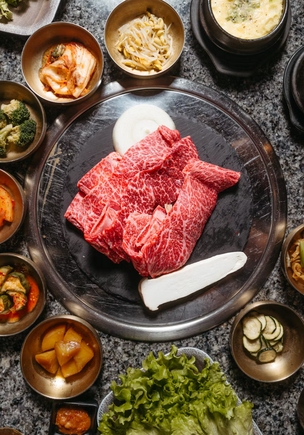 Raw beef on a stone plate with various side dishes around
