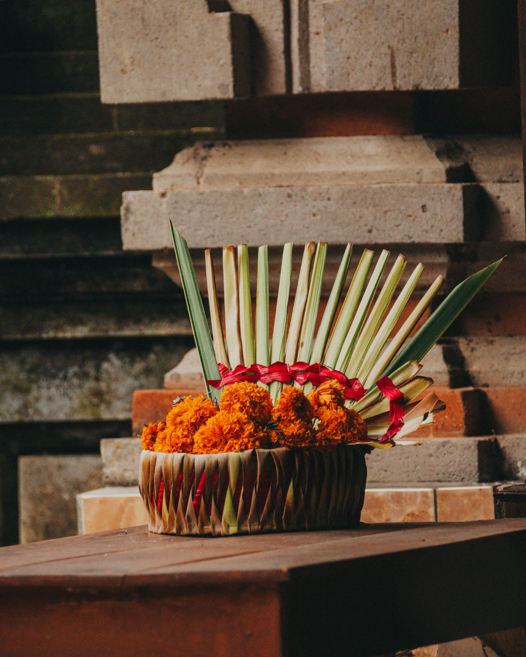 Bowl with marigold flowers and palm leaves on a stone step background