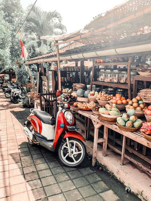 Outdoor market stall with various fruits and a scooter parked nearby.