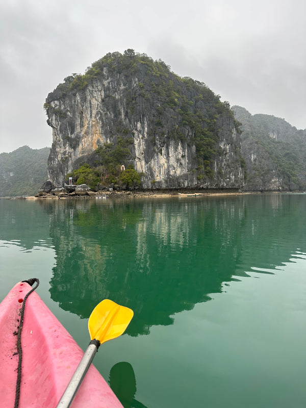 Kayak with a yellow paddle on a body of water with a large rock formation in the background.