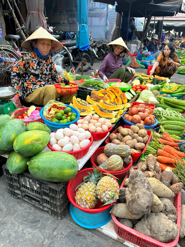 Three women selling fresh produce at an outdoor market.